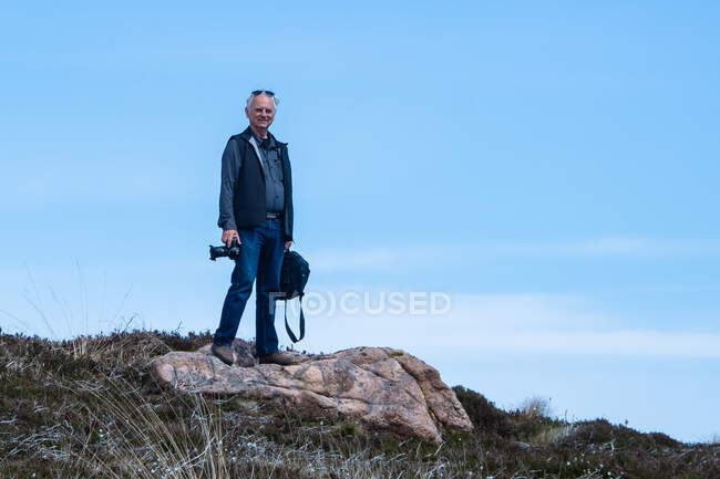 Homme debout sur un rocher tenant une caméra, Écosse, Royaume-Uni — Photo de stock