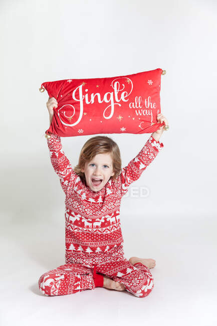 Portrait of a happy boy in pyjamas holding a Christmas pillow above his head — Stock Photo