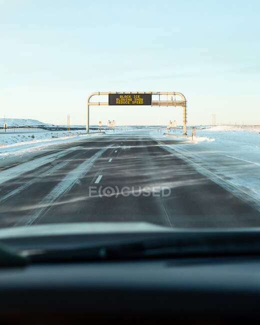 Carro dirigindo em direção a um aviso de sinal de estrada de gelo preto e neve soprando, EUA — Fotografia de Stock
