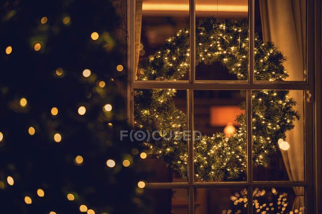 Vue à travers une fenêtre d'une couronne de Noël dans un salon — Photo de stock