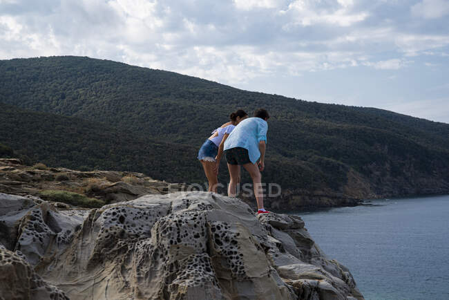 Man and woman standing on rocks looking down into the sea, Gulf of Baratti, Italy — Stock Photo