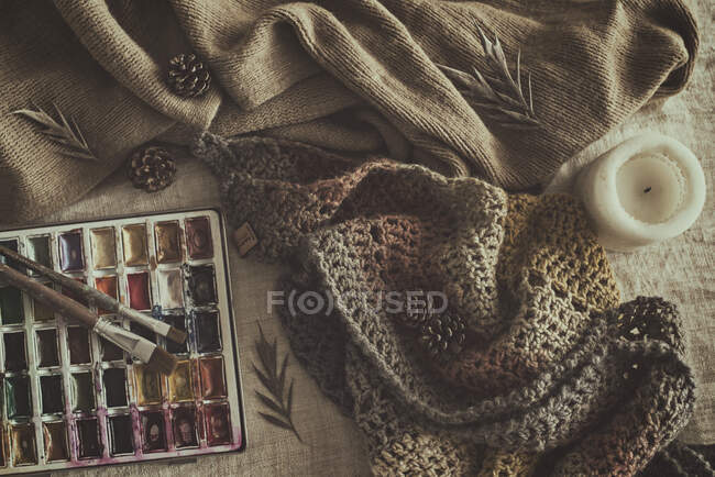 Watercolour paints and paintbrushes next to a candle and scarf — Stock Photo