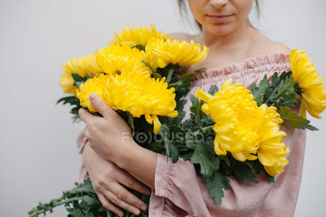 Femme souriante tenant un bouquet de chrysanthèmes jaunes — Photo de stock