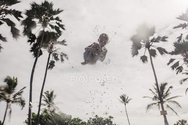 Vista de bajo ángulo de un niño siendo arrojado al aire en una piscina, Hawaii, EE.UU. - foto de stock