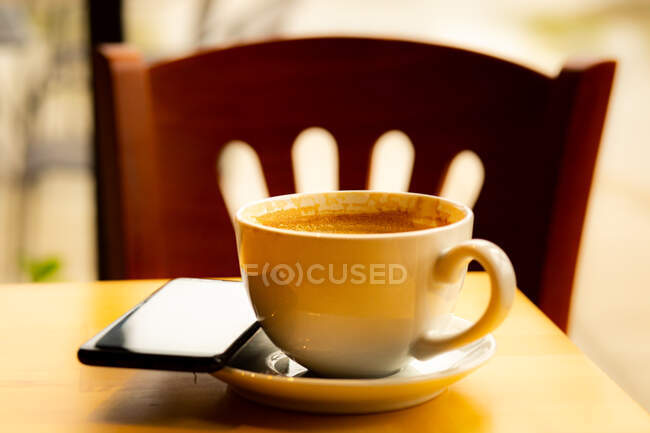 Taza de café y teléfono móvil en una mesa en una cafetería - foto de stock