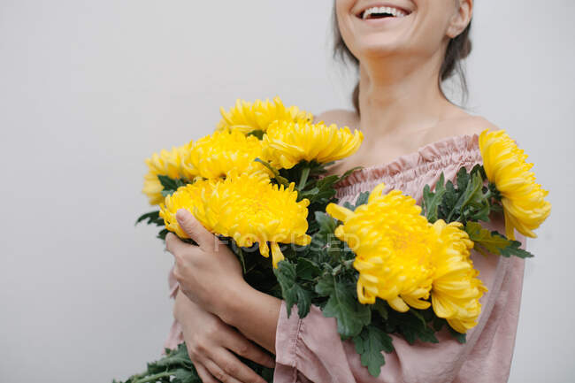 Mulher sorridente segurando um buquê de crisântemos amarelos — Fotografia de Stock