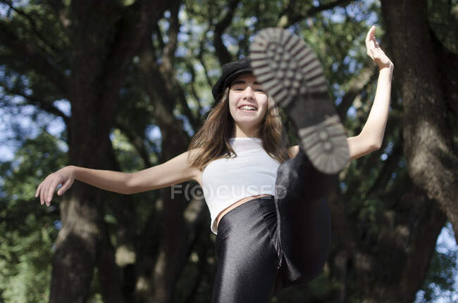 Smiling teenage girl standing in a park kicking her leg in the air, Argentina — Stock Photo