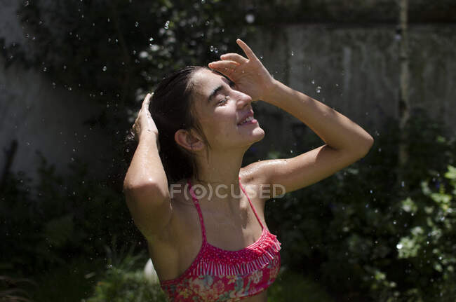 Teenage girl standing in a garden cooling off under a water sprinkler, Argentina — Stock Photo