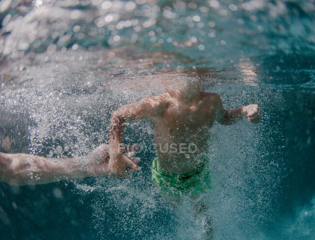 Мальчик плавает в бассейне, держа маму за руку. — стоковое фото