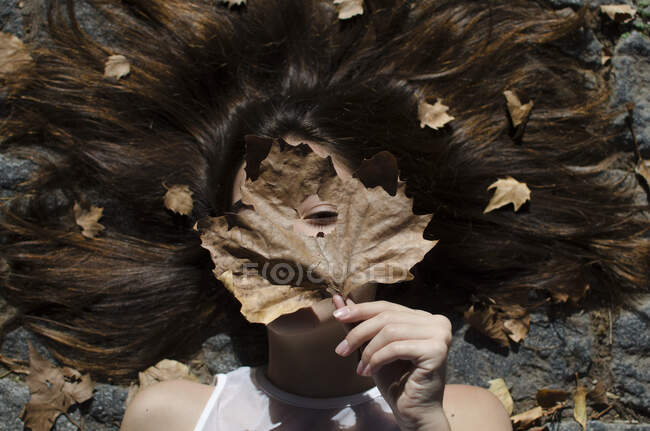 Adolescente acostada en el suelo con hojas en el pelo - foto de stock