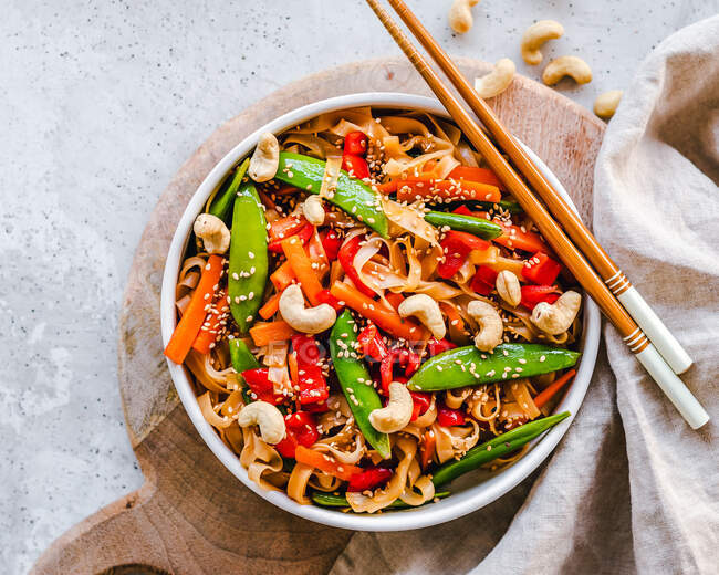 Stir fried noodles with mange tout, carrot, red pepper, sesame seeds and cashew nuts — Stock Photo