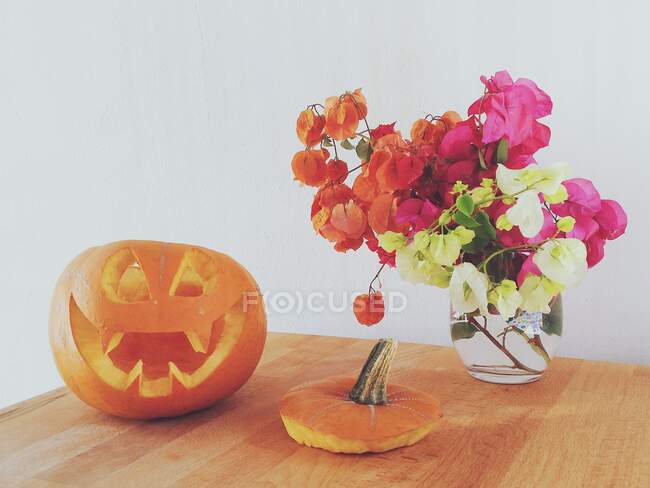 Jack-o-lantern next to a vase of flowers on a table — Stock Photo