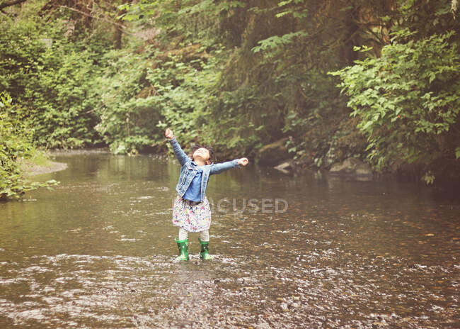 Улыбающаяся девушка, стоящая в ручье с распростертыми руками, США — стоковое фото