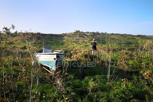 Человек, стоящий рядом со старой лодкой, Меллиха, Мальта — стоковое фото