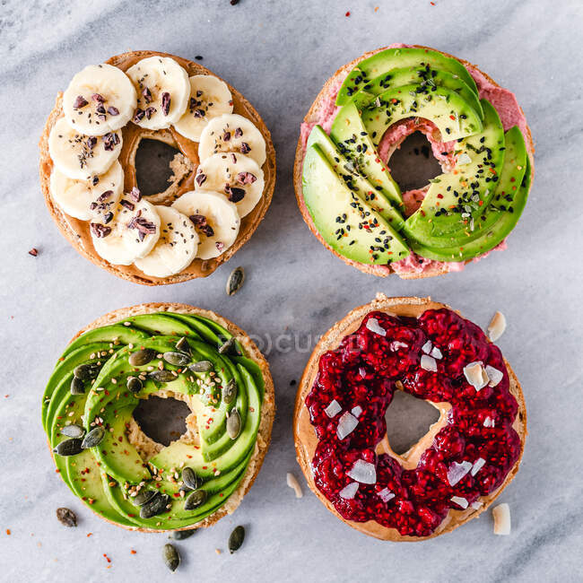 Four bagels topped with hummus, avocado, peanut butter, jam and banana — Stock Photo