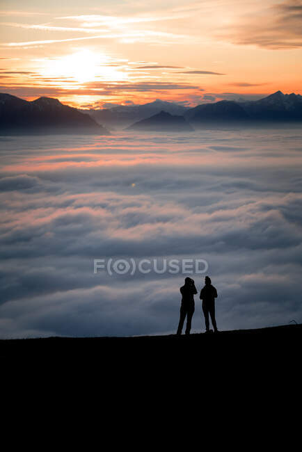 Силует двох жінок на вершині гори під час заходу сонця, дивлячись на вид, Зальцбург (Австрія). — стокове фото