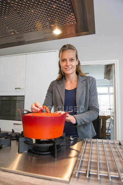 Woman standing in a kitchen next to a saucepan on a stove — Stock Photo