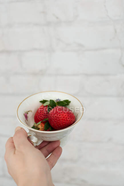 Woman's hand holding a cup of strawberries — Stock Photo