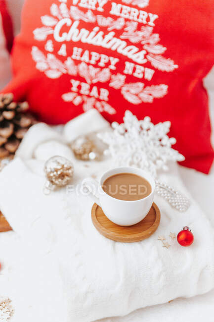 Cup of coffee next to a Christmas pillow and decorations — Stock Photo