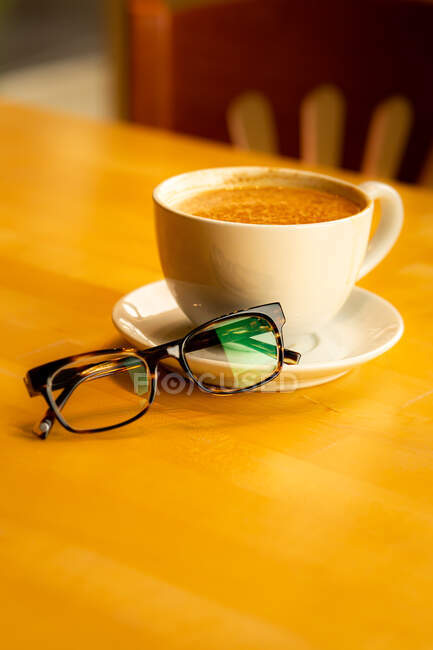 Spectacles next to a cup of coffee on a table — Stock Photo