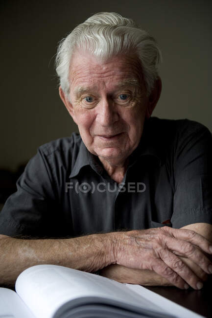 Portrait of a senior man sitting at a table with a book in front of him — Stock Photo