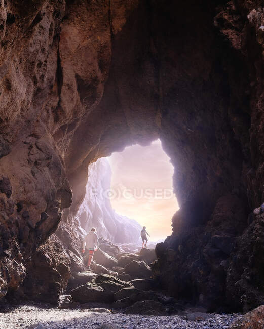 Two boys walking through a cave at sunset, Laguna Beach, California, USA — Stock Photo