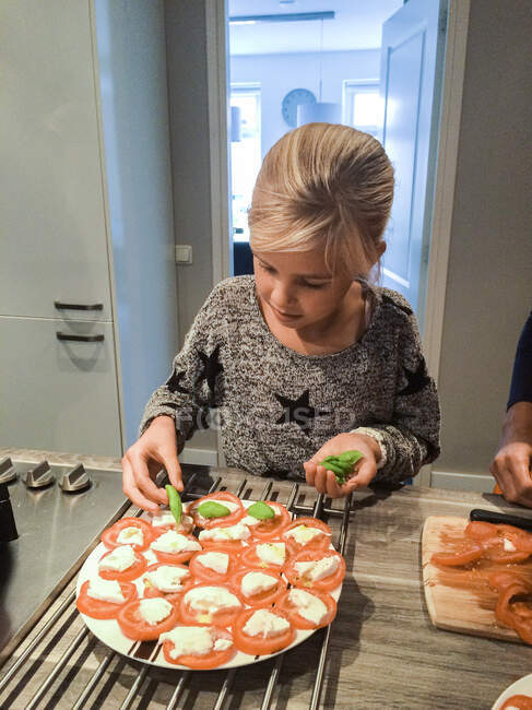 Chica de pie en la cocina preparando una ensalada caprese - foto de stock