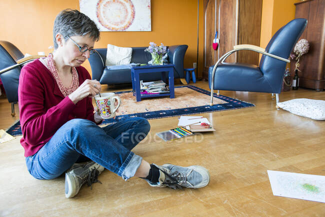 Ritratto di donna matura seduta a gambe incrociate sul pavimento con una bevanda calda — Foto stock