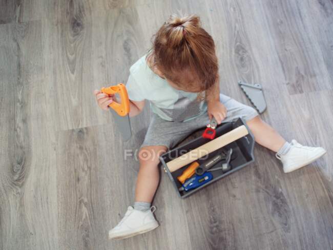 Дівчина сидить на підлозі, граючи з іграшковою коробкою для інструментів — стокове фото