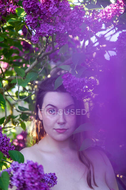 Retrato de una hermosa mujer de pie entre flores lila púrpura, Inglaterra, Reino Unido - foto de stock