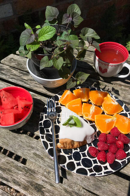 Té de menta con fruta fresca y una rebanada de pastel en una mesa de jardín, Inglaterra, Reino Unido - foto de stock