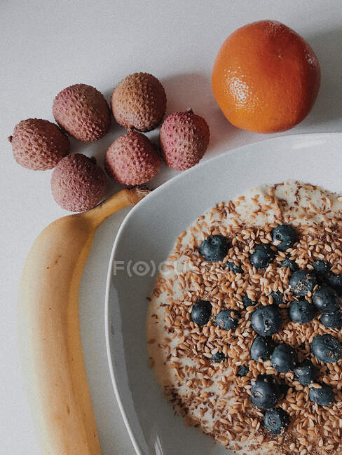 Oatmeal breakfast with blueberries and linseeds next to fresh fruit — Stock Photo