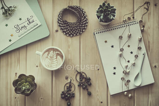 Kaffeetasse mit Schmuck, Pflanzen und Notizblöcken auf einem Tisch — Stockfoto