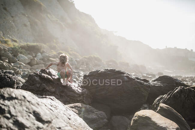 Boy climbing down rocks on beach, Laguna Beach, California, Estados Unidos - foto de stock
