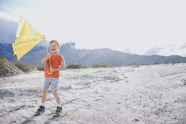 Смеющийся мальчик, стоящий в пустыне со сломанным зонтиком, Палм-Спрингс, Калифорния, США — стоковое фото