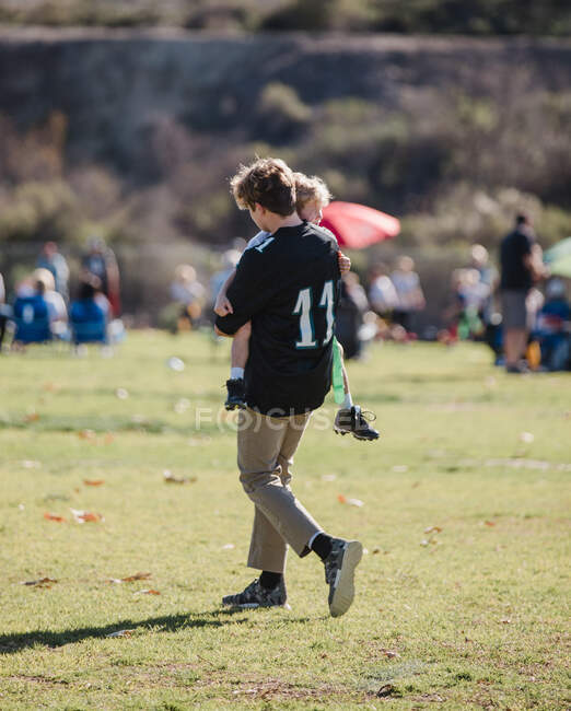 Хлопчик, який носив свого молодшого брата з футбольного поля після травми (штат Каліфорнія, США). — стокове фото