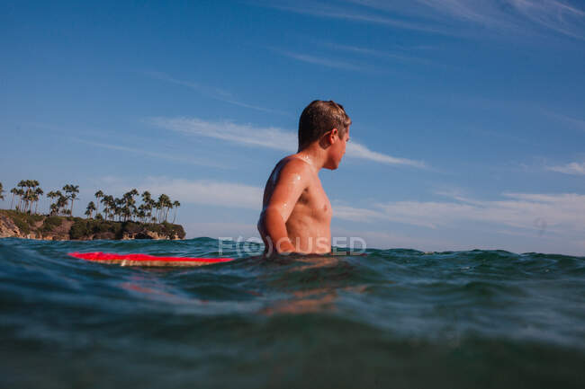 Adolescente sentado en una tabla de surf en el océano, Laguna Beach, California, Estados Unidos - foto de stock