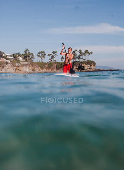 Adolescente parado en una tabla de surf remando, Laguna Beach, California, Estados Unidos - foto de stock