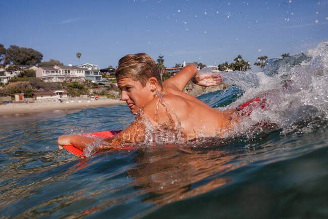 Jeune garçon pagayant sur un bodyboard dans l'océan, Laguna Beach, Californie, États-Unis — Photo de stock