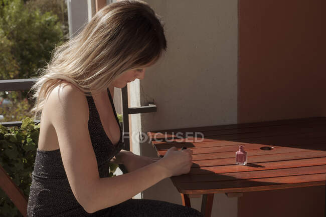 Mujer sentada en una mesa poniendo barniz de uñas - foto de stock