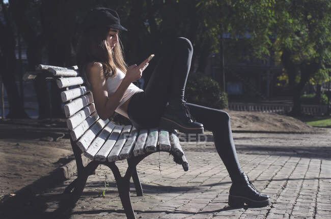 Девушка-подросток сидит на скамейке и смотрит на свой мобильный телефон, Аргентина — стоковое фото