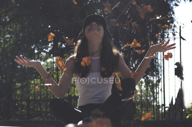 Adolescente assise sur le sol jetant des feuilles dans les airs, Argentine — Photo de stock