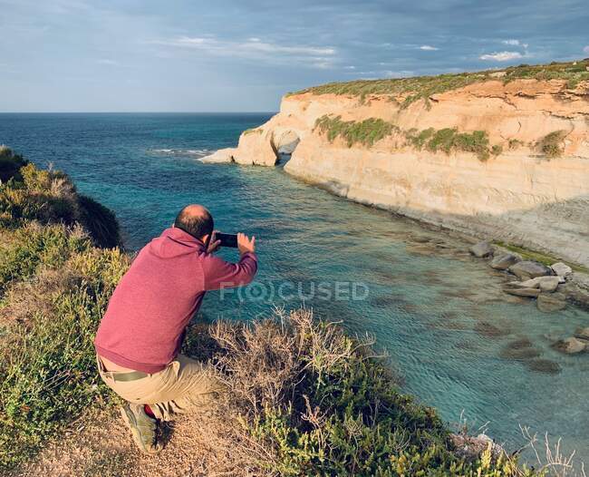 Мужчина, стоящий у моря и фотографирующий, Мунксар, Марсаскала, Мальта — стоковое фото
