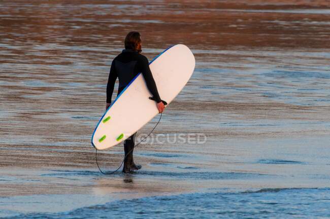 Hombre parado en la playa llevando una tabla de surf, Tofino, Vancouver, Columbia Británica, Canadá - foto de stock
