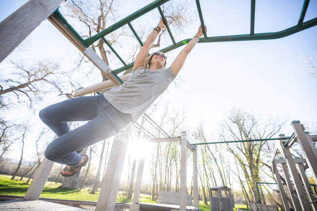 Woman playing on monkey bars in a playground, United States — Stock Photo