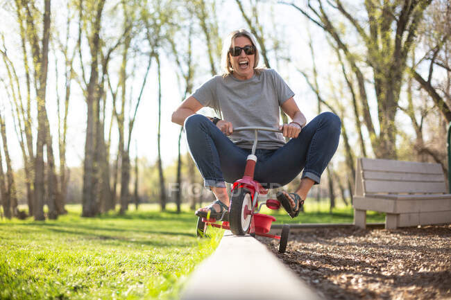 Женщина играет на трехколесном велосипеде в парке, США — стоковое фото