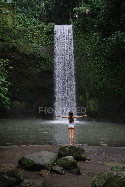 Donna in piedi su una roccia da una cascata con le braccia tese, Indonesia — Foto stock