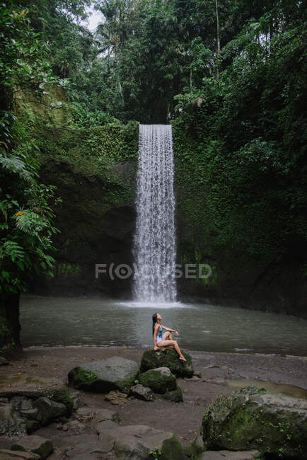 Frau sitzt auf Felsen neben einem Wasserfall, Bali, Indonesien — Stockfoto