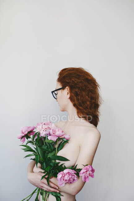 Porträt einer jungen Frau mit Brille, die Pfingstrosen hält und ihr über die Schulter schaut — Stockfoto