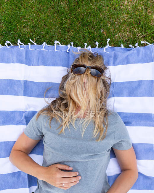 Femme couchée sur une couverture dans le jardin avec ses cheveux couvrant son visage — Photo de stock